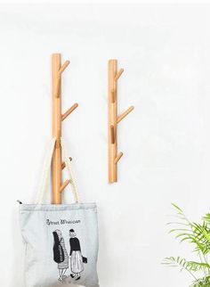 two wooden clothes pegs are hanging on the wall next to a canvas bag and potted plant