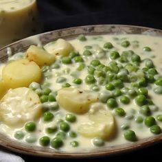 a bowl filled with peas and potatoes on top of a table next to a glass of milk