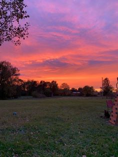 the sky is pink and purple as the sun sets over an open field with trees in the foreground