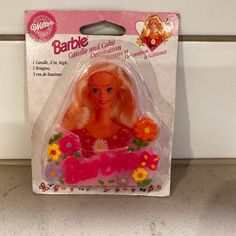 the barbie doll is in its package on the counter top with flowers and daisies