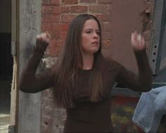 a woman standing in front of a brick wall with her hands up to the side