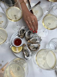 a table topped with oysters next to wine glasses and plates filled with saucers