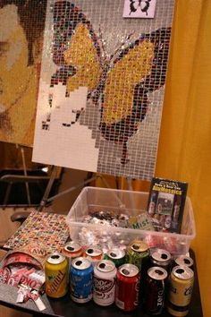 an assortment of sodas and cans on a table in front of a mosaic wall