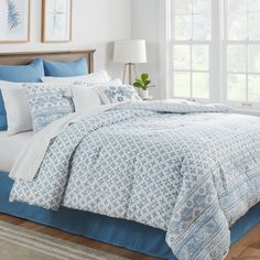 a bed with blue and white comforters in a bedroom next to a window on a wooden floor