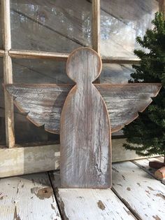 a wooden angel ornament next to a small christmas tree in front of a window