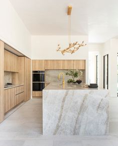 a large kitchen with marble counter tops and wooden cabinetry, along with a chandelier hanging from the ceiling