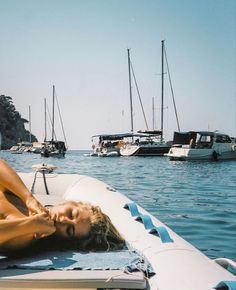 a woman laying on top of a boat in the ocean next to other boats and yachts