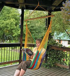 a woman sitting in a hammock reading a book on the porch with her feet propped up