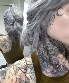 a woman with grey hair has tattoos on her neck and shoulder, while she is looking in the mirror