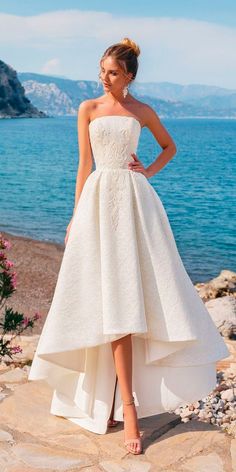 a woman in a white dress is standing on the rocks by the water with her hands on her hips