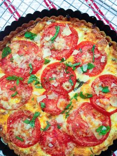 a pizza with tomatoes, cheese and basil on top is sitting on a wire rack