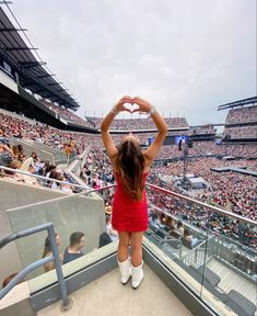 a woman in a red dress holding up a heart shaped object at a baseball game