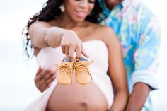 a pregnant woman holding a pair of baby shoes while standing next to a man in a blue shirt