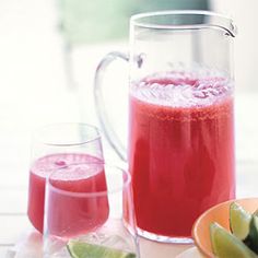 a pitcher and two glasses filled with red liquid next to sliced fruit on a table