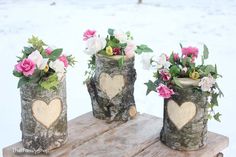 three wooden vases with flowers in them sitting on a wood table outside during the day