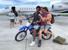 two men sitting on a motorcycle in front of an airplane