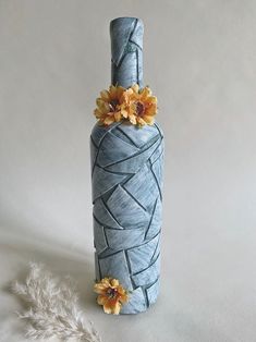 a blue vase with yellow flowers in it on a white tablecloth and feathers next to it