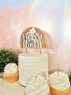 two cupcakes sitting on top of a table next to a white cake with frosting