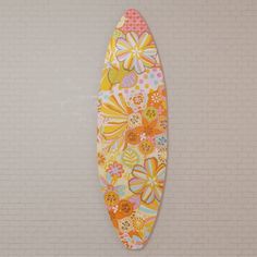 a colorful surfboard hanging on the wall in front of a white brick wall with flowers painted on it