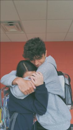 two people hugging each other in front of a red wall