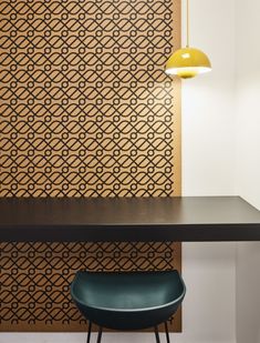 a black table with a green chair and a yellow lamp on it in front of a patterned wall