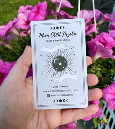 a person holding up a card with the moon and sun on it in front of pink flowers