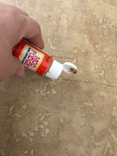 a hand holding a tube of glue on top of a tile floor next to a wall