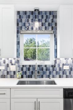 a kitchen with white cabinets and blue tiled backsplash, window above the sink