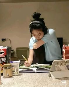 a woman sitting at a table writing on a book with a pencil in her hand