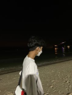 a man walking on the beach at night with a face mask covering his mouth and nose