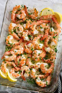 a glass dish filled with shrimp and garnished with parsley, lemon wedges