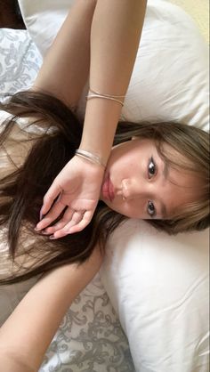 a woman laying on top of a bed with her hair blowing in the wind and wearing bracelets