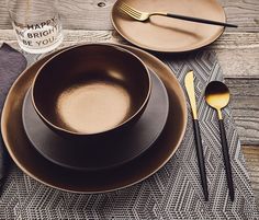 the table is set with black and gold plates, utensils and silverware