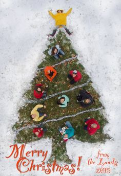 a group of people standing around a christmas tree in the snow with an orange and yellow sign that says merry christmas