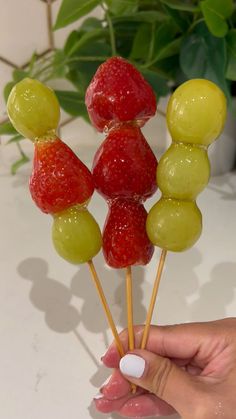 a person is holding some fruit on a stick with gummy bears and strawberries