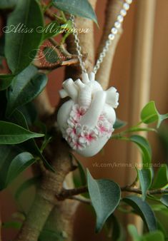 a white necklace with pink flowers hanging from it's side on a tree branch