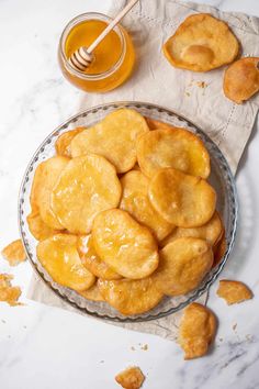 a glass bowl filled with fried doughnuts next to a cup of honey