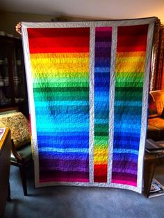 a large rainbow quilt hanging from the ceiling in a room with a chair and table