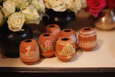 several vases with designs on them are sitting on a table next to roses and other flowers