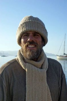 a man with a beard wearing a knitted hat and scarf by the water's edge