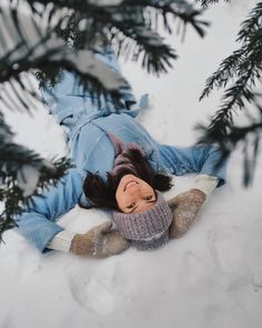 a woman laying in the snow next to a pine tree