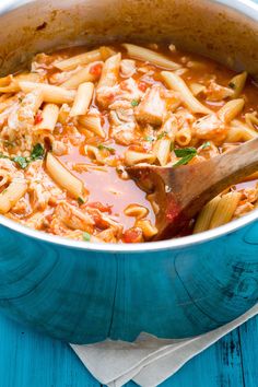 a blue pot filled with pasta and meat in tomato sauce on top of a wooden table