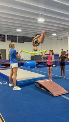 two girls are doing tricks on the trampoline in an indoor gym while others watch