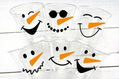 four glasses with faces painted on them sitting in front of a white wooden table top