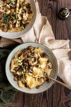 two bowls filled with pasta and mushrooms on top of a wooden table next to a napkin