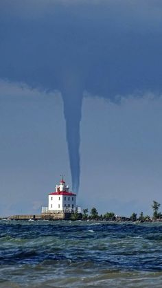 a funnel cloud is seen over the ocean with a lighthouse in the background