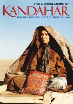 a woman sitting on top of a stone wall next to a blanket and pillow in the desert