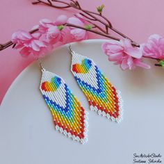 a pair of colorful beaded earrings on top of a white plate next to pink flowers