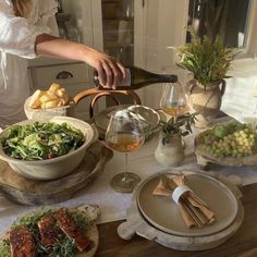 a person pouring wine into a bowl filled with salad and other foods on a table