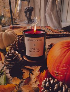 a candle sitting on top of a wooden table next to pumpkins and pine cones